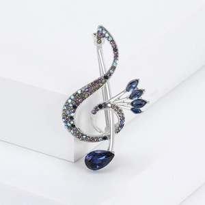 Detailed view of music note brooch with silver metal, blue gemstones and colorful rhinestones