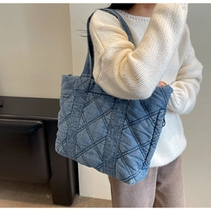 Détail du grand sac cabas en denim matelassé bleu porté à l'épaule par une femme