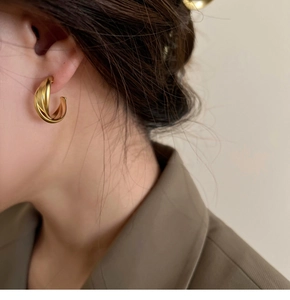Détail de boucles d'oreilles clips dorées mates croisées sur mannequin au design français