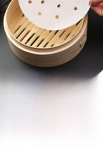 Close-up of white perforated silicone steaming paper liners inside a bamboo steamer basket