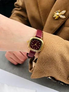 Détail d'une montre à quartz dorée vintage avec bracelet en cuir bordeaux et cadran rouge