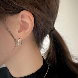Close-up of a minimalist sterling silver hoop earring worn by a model in a natural setting