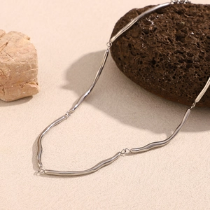 Detailed view of silver stainless steel wavy bamboo chain on a textured stone surface