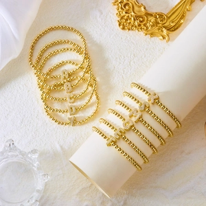 Close-up of golden beaded bracelets featuring micro-set zircon initial letter pendants