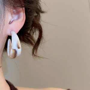 Close-up of a model wearing C-shaped acrylic hoop earrings with brown tortoise pattern