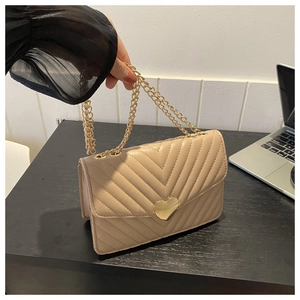 Dettaglio borsa trapuntata beige con chiusura a cuore dorata e tracolla a catena su tavolo