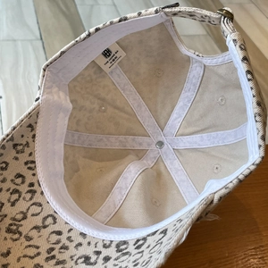 Detail view of the stitching, metal button, and internal label on leopard print cap