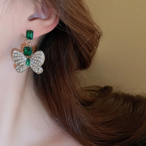 Gros plan détaillé d'une boucle d'oreille papillon dorée avec gemme verte et cristaux