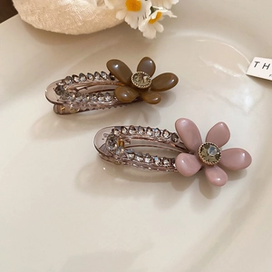 Detail view of two acrylic flower hair clips with rhinestones and gems in a tray