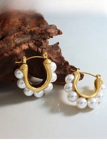 Close-up of gold-plated U-shaped earrings with white pearls on a natural stone surface