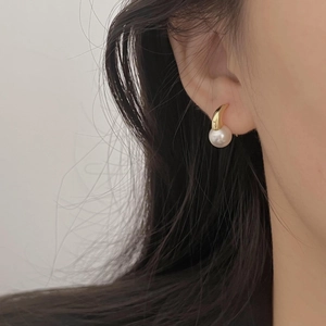 Detailed close-up of a minimalist gold pearl earring worn by a model in soft lighting