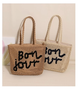 Detail of woven straw tote bags in beige and brown with Bonjour embroidery for beach holidays