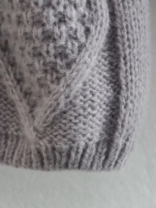 Dettaglio del maglione grigio in maglia a rombi con trama spessa e finitura morbida