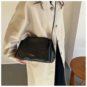 Detail of the black leather shoulder bag with metal chain strap worn by a model