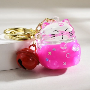 Detail of pink lucky cat keychain with moving liquid glitter and a red bell accessory