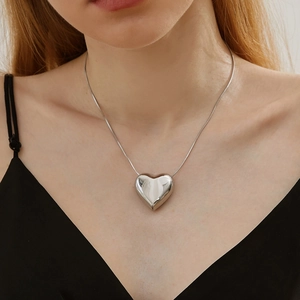 Polished silver heart pendant necklace on minimalist snake chain worn by a female model