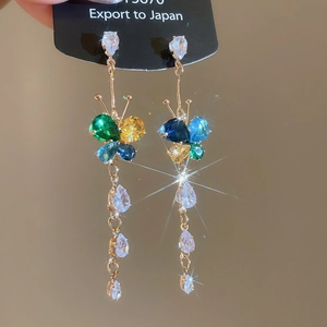 Macro view of butterfly earrings with zircon stones and long tassels on a black card