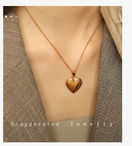 Detail of gold heart pendant necklace with scroll relief on a model wearing a grey blazer