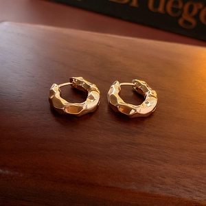 Detail of gold-plated hoop earrings with irregular hammered texture on dark wood