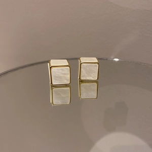 Vue détaillée de boucles d'oreilles cubiques dorées avec nacre et reflet sur un miroir