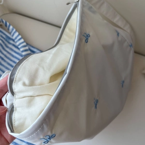 Détail de la broderie de nœud bleu sur le sac bandoulière en coton blanc à fermeture éclair