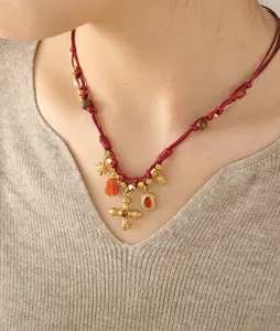 Detail of bohemian red cord necklace with gold cross pendant and red agate stones on model