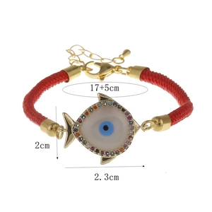 Detail of red cord bracelet with gold shell fish charm and evil eye zircon stones