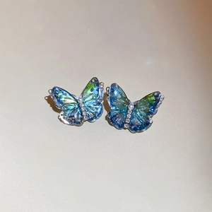 Macro detail of butterfly earrings with blue-green resin gradient and gold foil flakes