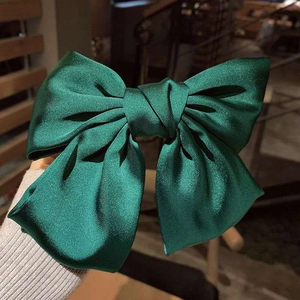 Macro shot of large dark green satin bow hair clip with elegant pearl luster finish