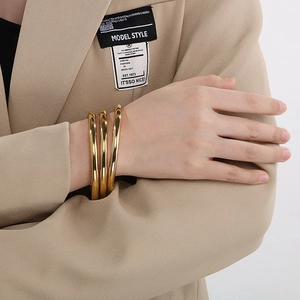 Close-up of three stacked 18k gold plated chunky 6mm hoop bracelets on a model's wrist