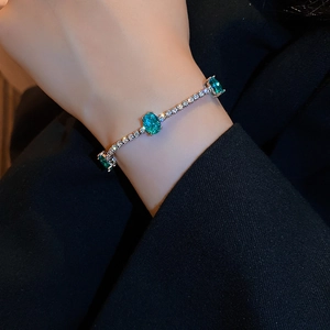 Close-up of silver bracelet with green oval gemstone and white zircon on wrist