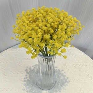 Detail of yellow artificial gypsophila flowers in a striped glass vase on lace