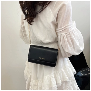Detail view of black textured leather chain bag worn with a white ruffled dress