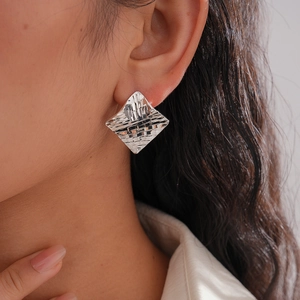 Close-up of silver geometric rhombus earrings with intricate woven texture on a model