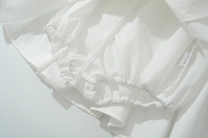 Détails d'une robe blanche en polyester montrant la texture froncée et les finitions