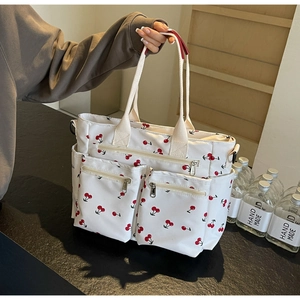 Detail view of white canvas tote bag with cherry print and multiple functional zip pockets