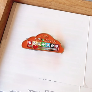 Macro detail of orange cloud mood tracker enamel pin with a sliding red heart indicator