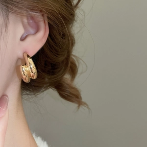 Close-up of golden cross curved earrings on ear with high mirror polished finish