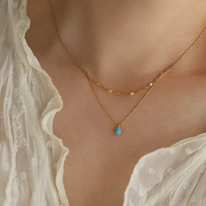 Gros plan d'un collier double épaisseur plaqué or avec un pendentif opale bleue en goutte