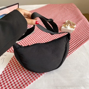 Detailed view of black nylon crescent bag with adjustable wide strap on a plaid background