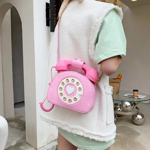 Pink retro telephone-shaped crossbody bag in glossy patent leather worn by a model