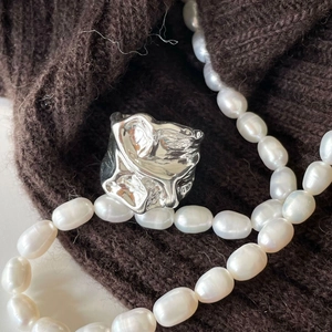 Close-up of irregular silver pleated wide ring on brown knit with pearl necklace accent