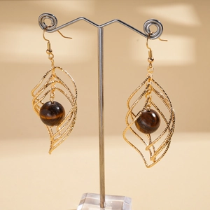 Detail of geometric golden textured cage earrings with polished tiger eye stone beads