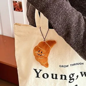 Plush croissant keychain with a cute smiling face attached to a canvas backpack