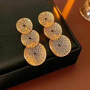 Goldene, hohle, gestufte Rundohrringe mit filigranem Design auf schwarzem Lederhintergrund