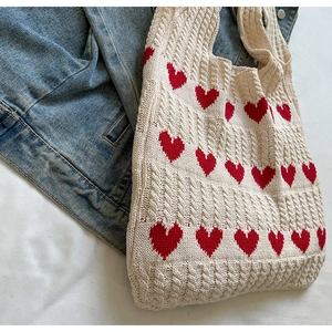 Detalle del tejido de ochos de un bolso crema con patrones de corazones rojos y denim