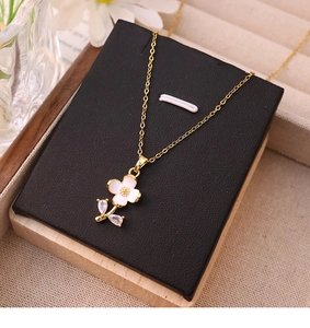 Close-up of golden titanium necklace featuring white enamel flower pendant and zircon stones
