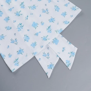 Detailed close-up of white dress fabric featuring light blue floral patterns and tie-dye bow