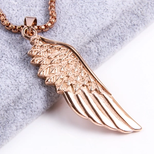 Macro shot of rose gold angel wing pendant with detailed feathers on soft gray plush fabric