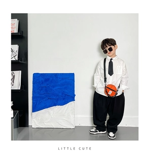 Garçon en chemise blanche et pantalon noir avec un petit sac à bandoulière rond orange vif